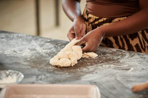 Person braiding dough on a flour-dusted countertop, with a baking dish nearby.